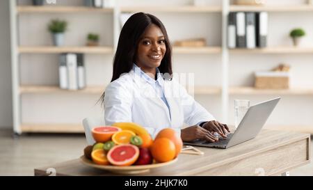 Concetto di nutrizione sana. African american consulente di perdita del peso che digita sul computer portatile, dando la consultazione in linea Foto Stock