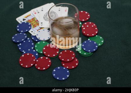 Un bicchiere di whiskey con ghiaccio sulle rocce con chip da poker e una mano di carte su sfondo verde brasato Foto Stock