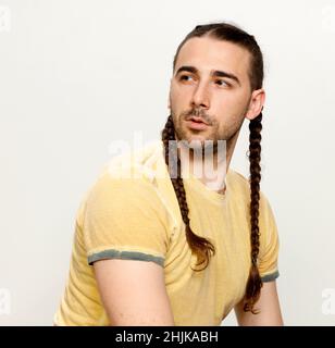 Modello maschile elegante con trecce in posa in studio su sfondo isolato. Stile, acconciatura, concetto di moda. Foto Stock