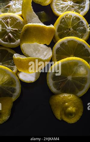 fette di limone e buccia intera di limone arricciate a spirale su uno sfondo di vetro nero glittery Foto Stock