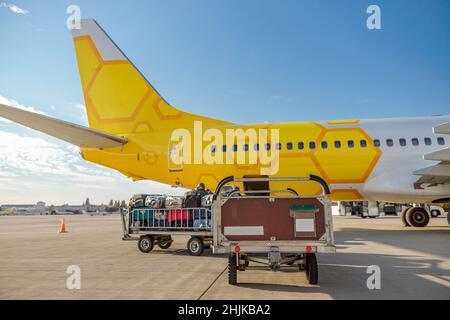 Aereo passeggeri giallo e carretto bagagli con borse da viaggio sotto il cielo blu all'aeroporto Foto Stock