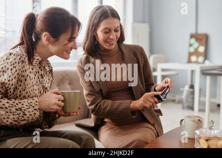 Donna incinta felice che mostra la scansione del suo bambino al suo collega mentre bevono caffè durante la pausa in ufficio Foto Stock