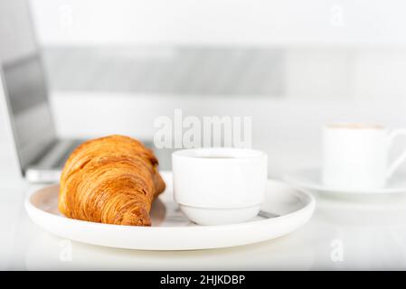 Caffè, croissant e computer portatile sul tavolo. Colazione. Foto Stock