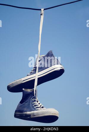 Vecchie sneakers appese su un cavo elettrico su uno sfondo cielo chiaro Foto Stock