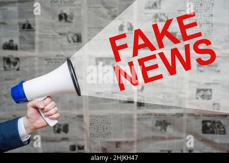 Man's Hand Holding Megaphone con Speech Bubble FALSE NOTIZIE su Quotidiani sfondo. Foto Stock