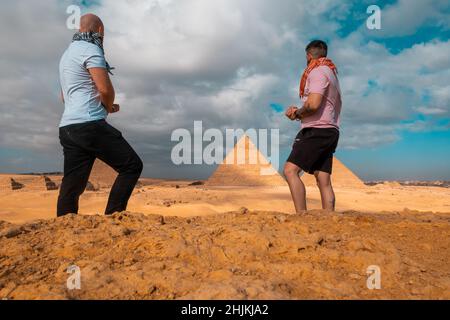Due uomini viaggiatori in posa di fronte alle grandi piramidi di giza al cairo egitto. Viaggiando in egitto durante l'inverno, freddo inverno giorno coperto. Foto Stock