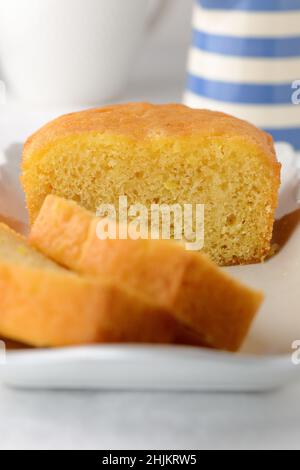 Torta fatta in casa per il tè del pomeriggio, tagliata a fette su un piatto rettangolare bianco con caraffa a righe blu e bianca sullo sfondo Foto Stock