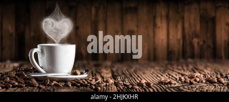 Tazza da caffè bianca e piattino con vapore a forma di cuore su tavolo in legno Foto Stock