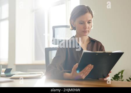 Ritratto di giovane donna che legge documenti in ufficio illuminato dalla luce del sole, spazio copia Foto Stock