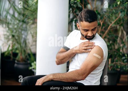 Prevenzione della vaccinazione contro la diffusione del covid 19 e dell'influenza. Un giovane ragazzo indiano che vaccina contro il coronavirus controlla la condizione della sua mano dopo la vaccinazione, guarda il cerotto sulla sua mano Foto Stock