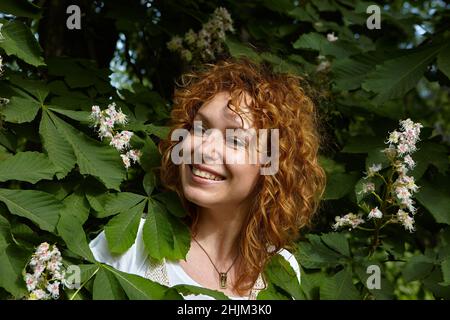 Ritratto di bella donna capelli rossi con sorriso raggiante tra i fiori di castagno. Foto Stock