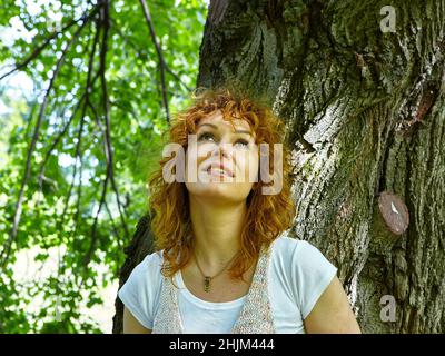 Romantico Ritratto di bella donna capelli rossi in ombra di albero guardando in su Foto Stock