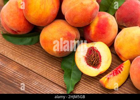 Pesche mature e foglie su tavola di legno. Frutta fresca pesche con foglie su sfondo di legno. Foto Stock