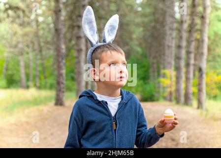 Un bambino alla ricerca di uova di Pasqua nella foresta. Ragazzino a caccia di uova di Pasqua in legno di primavera il giorno di Pasqua. Il concetto di caccia alle uova di Pasqua. Foto Stock