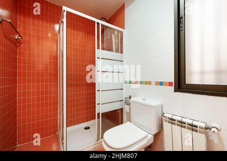 Bagno piastrellato con piastrelle rosse, bordo colorato e doccia bianca con divisorio in vetro Foto Stock