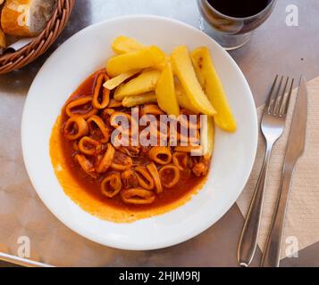 Anelli di calamari stufati in americaina salsa servita con patatine fritte Foto Stock