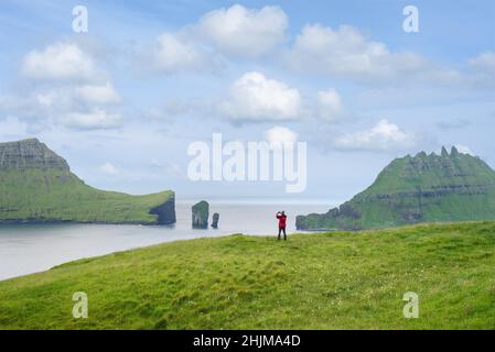 Un turista fotografa una vista delle pile di mare di Drangarnir e l'isolotto di Tindholmur Foto Stock