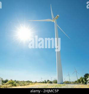 Enorme generatore di vento contro il sole splendente e il cielo blu. Allevamento eolico di Oreites a Cipro Foto Stock