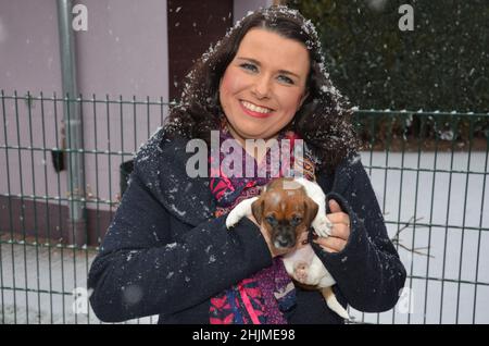 La donna felice tiene un cucciolo di tre settimane di Jack Russell Terrier tra le braccia. In inverno con nevicate. Foto Stock