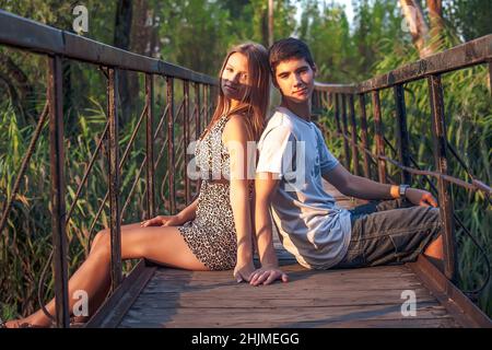 Una coppia innamorata si siede su un ponte di legno con ringhiere arrugginite. Una giovane coppia felice cammina nella natura e gode di comunicazione. Foto Stock