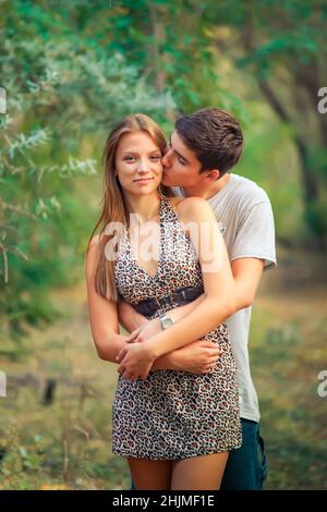 ragazzo in amore bacia la sua padrona che la abbraccia da dietro Foto Stock