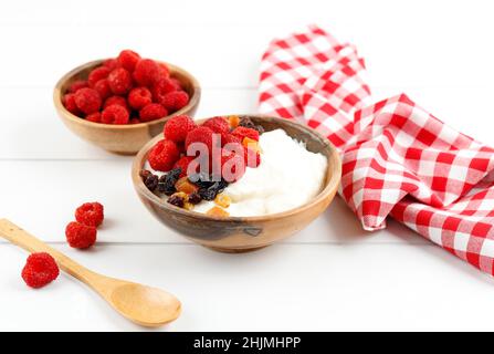 Ciotola di legno di yogurt greco panna montata con lamponi e frutta secca, primo piano su sfondo bianco Foto Stock