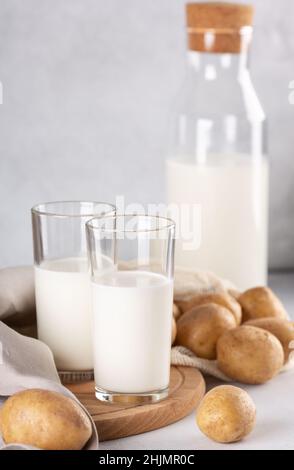 Latte vegetale vegano in due bicchieri trasparenti e bottiglia. Latte di patate e tuberi di patate alternativi su tavola grigia Foto Stock