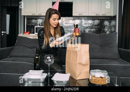 Festa di compleanno a casa, donna ha ordinato cibo online e scompack pacchetto dal ristorante, consegna stoviglie usa e getta con cena Foto Stock