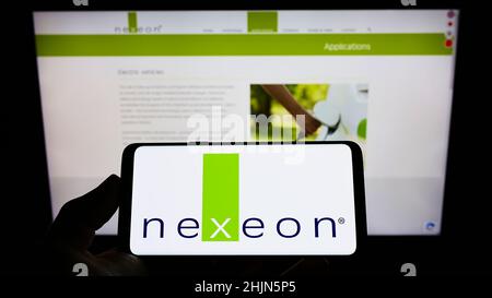 Persona che tiene il cellulare con il logo della società britannica di batterie Nexeon Ltd. Sullo schermo di fronte al sito web aziendale. Mettere a fuoco sul display del telefono. Foto Stock