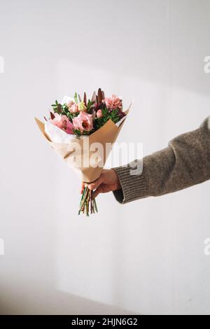 Giovane donna in maglia grigia con bouqet di fiori in mano sullo sfondo grigio Foto Stock