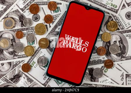 Smartphone con logo Wells Fargo banca circondato da una varietà di monete metalliche sullo sfondo di bollette in dollari Foto Stock