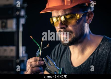 Un elettricista maschio lavora in un quadro elettrico con un cavo di collegamento elettrico. Foto Stock