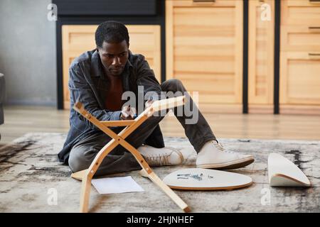 Ritratto a tutta lunghezza di giovane uomo afroamericano che monta mobili a casa, spazio copia Foto Stock