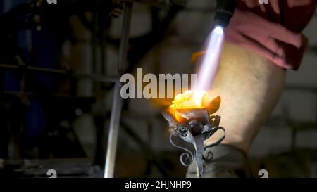 Il fabbro allinea le foglie di ferro rosa e fa la forma finale del fiore. Il fabbro fa rosa di ferro. Foto Stock