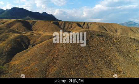 Vista ravvicinata delle colline di sabbia e ghiaia e delle gole vicino alle montagne ricoperte di arbusti verdi e alberi contro il cielo blu. Splendida montagna scener Foto Stock