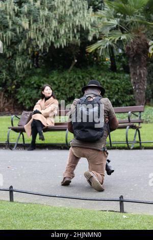 Il fotografo scatta una foto della ragazza seduta sulla panchina, St Stephen’s Green Park , urban, fotografia di strada, Dublino, Irlanda Foto Stock