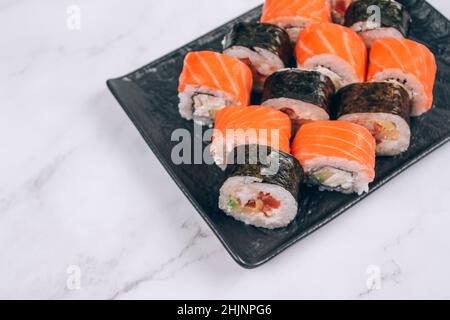 Menu per il pranzo al sushi bar, diversi sushi roll con salmone, avocado e anguilla affumicata su sfondo di tavolo di marmo bianco. Online ordinare cibo consegna online Foto Stock