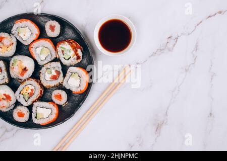 Menu pranzo al sushi bar, vista dall'alto - diversi sushi roll con salmone, avocado e anguilla affumicata su sfondo di tavolo di marmo bianco. Consegna degli ordini online Foto Stock