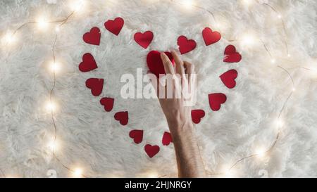 Guy prepara il cuore rosso con carta su tappeto bianco neve Foto Stock