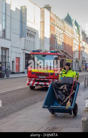 Fire Brigade camion in strada al mattino presto, al lavoratore anteriore con carriola in un gilet giallo, fotografia di strade, Dublino, Irlanda Foto Stock