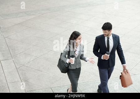 I giovani colleghi di affari positivi camminano all'aperto e discutono del progetto su cui stanno lavorando Foto Stock