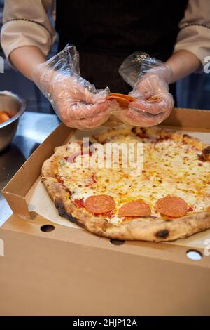 La macchina per la pizza mette gli ingredienti sull'impasto. Fare la pizza con salsiccia e salame Foto Stock