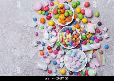 Draghe, caramelle, lecca lecca, marshmallows, dolci e brillanti per feste divertenti su sfondo grigio di cemento Foto Stock