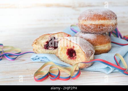 Berliner ciambelle anche chiamato Krappen riempito con marmellata su un tovagliolo con streamers partito, dolce pasticceria per il carnevale e Capodanno, sfondo di legno chiaro, Foto Stock