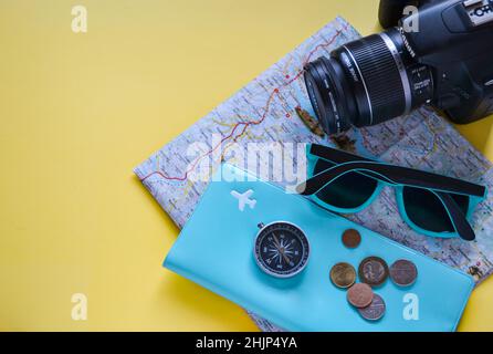 Mappa, fotocamera DSLR Canon, occhiali da sole con cornice blu, cartella per biglietti e documenti turchese con piano bianco, bussola, spazio copia Foto Stock