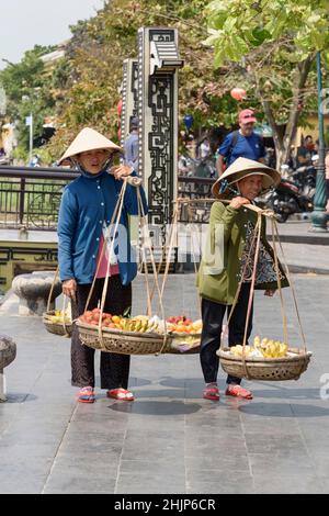 Le donne vietnamite venditori di cibo di strada che indossano cappelli conici tradizionali vendono frutta sulle strade di Hoi An, provincia di Quang Nam, Vietnam centrale Foto Stock