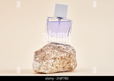 Bottiglia di profumo su podio in pietra naturale su sfondo beige, minimo spazio di riproduzione per il prodotto cosmetico di presentazione Foto Stock