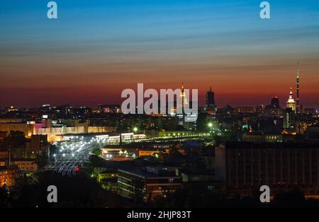Tramonto saturo di rosso e blu con nuvole chiare in città. Silhouette della città e luci della stazione ferroviaria e della ferrovia. Mosca, Russia. Foto Stock