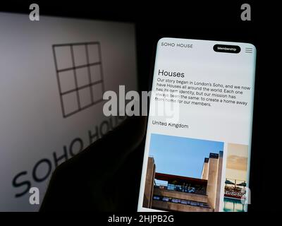 Persona che detiene il cellulare con il sito web della società di club britannico Soho House UK Limited sullo schermo di fronte al logo. Concentrarsi sul centro del display del telefono. Foto Stock
