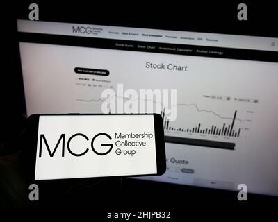 Persona che detiene il telefono cellulare con il logo della società di club Membership Collective Group Inc. (MCG) sullo schermo di fronte alla pagina Web. Mettere a fuoco sul display del telefono. Foto Stock